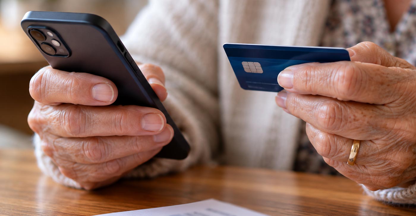 Mains d'une personne âgée qui tient un téléphone et une carte de crédit